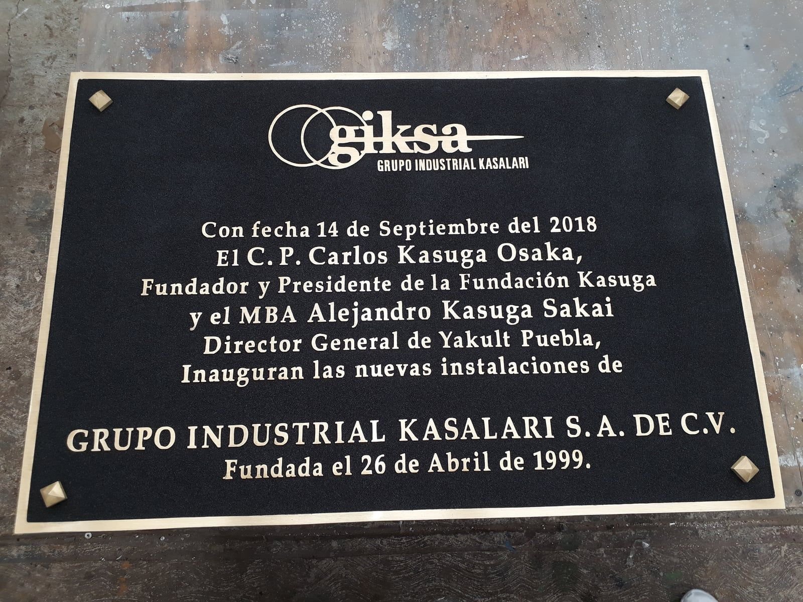 Placa de inauguración fundida en bronce para Grupo Industrial Kasalari, con texto en relieve sobre fondo negro y chapetones en las esquinas